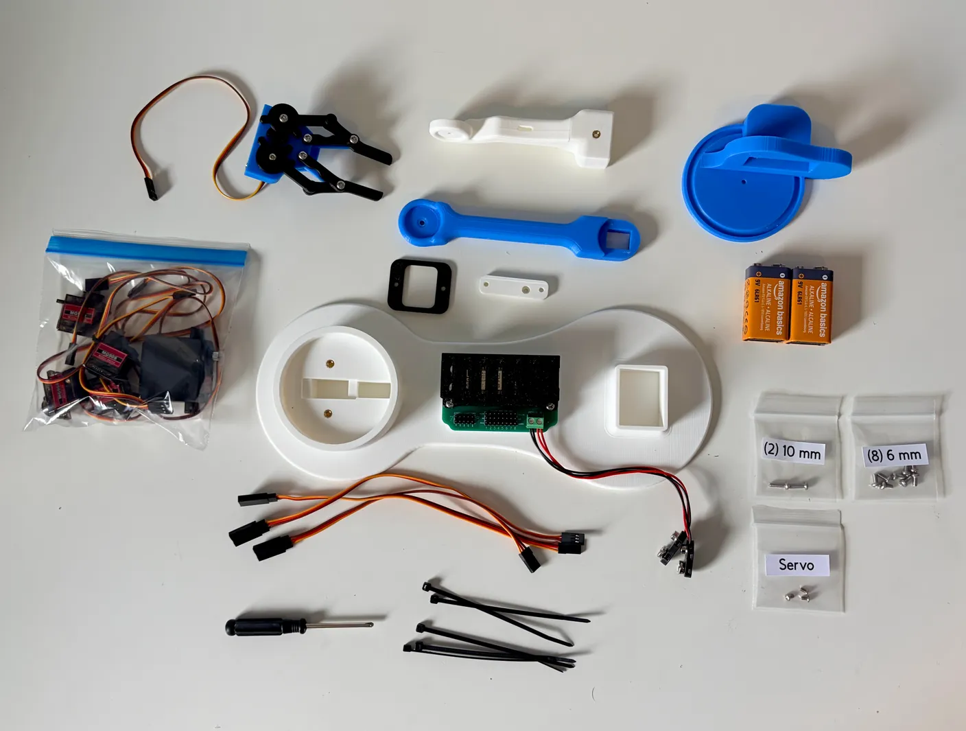 Robotic Arm build — Introduction: Everything included in the Robotic Arm Kit laid out — five servos, blue and white 3D-printed parts, the gripper, control board, two 9-volt batteries, a screwdriver, wiring, and zip ties.